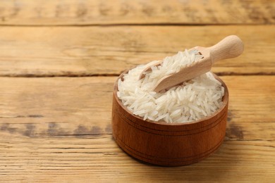 Photo of Raw basmati rice in bowl and scoop on wooden table, space for text
