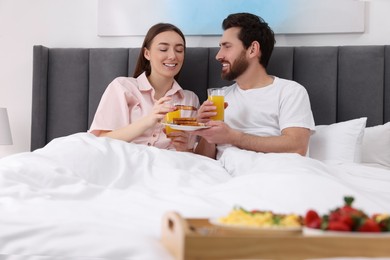 Happy couple eating tasty breakfast in bed at home