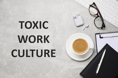 Image of Cup of coffee, computer keyboard, stationery and text TOXIC WORK ENVIRONMENT on grey table, flat lay 