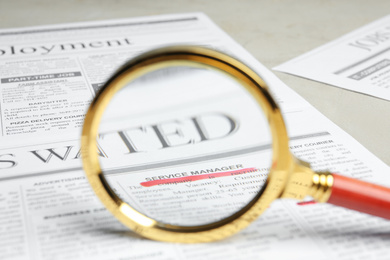 Photo of Looking through magnifying glass at newspaper, closeup. Job search concept