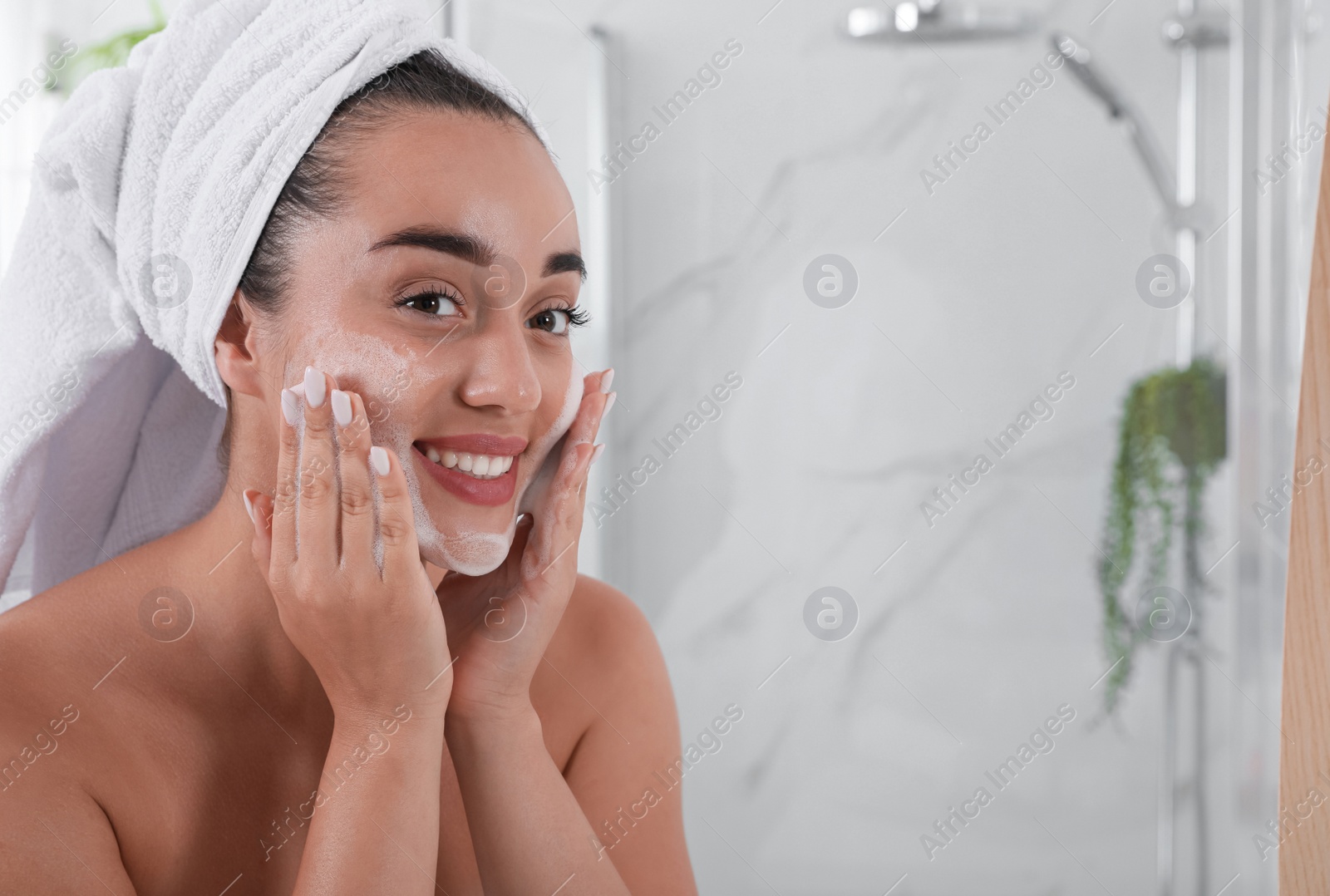 Photo of Beautiful young woman applying cleansing foam onto face in bathroom, space for text. Skin care cosmetic