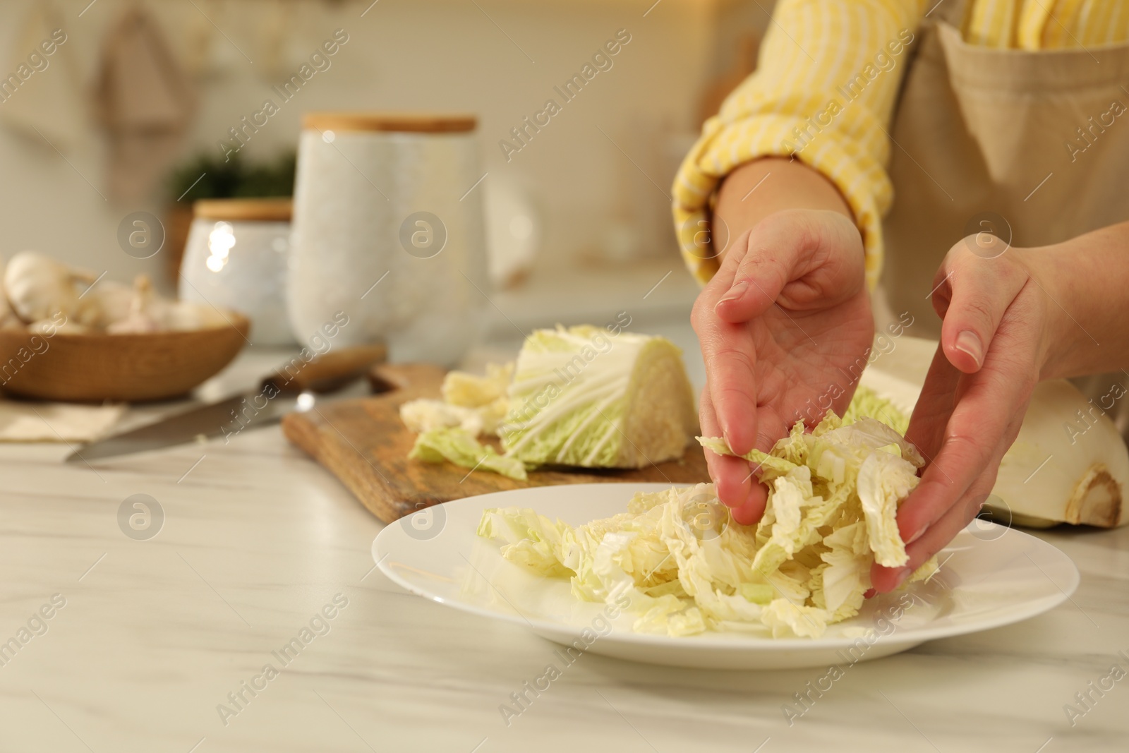 Photo of Woman putting cut Chinese cabbage into plate at white kitchen table, closeup