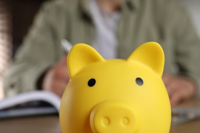 Man at table, focus on yellow piggy bank