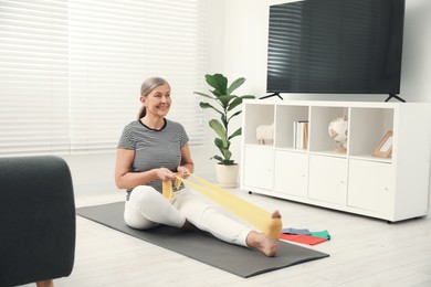 Senior woman doing exercise with fitness elastic band on mat at home