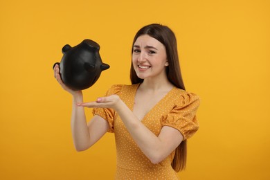 Sad woman with piggy bank on orange background