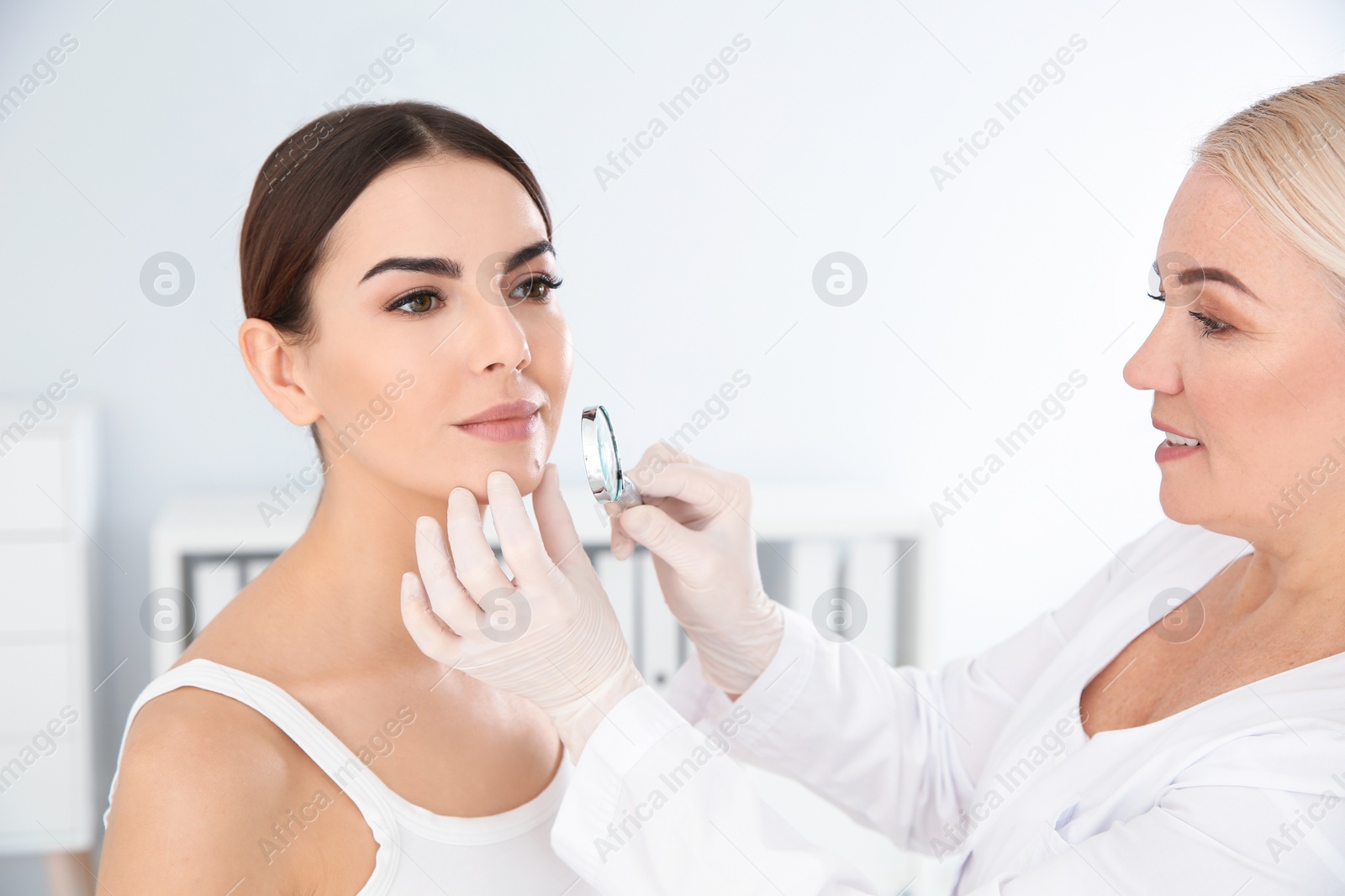Photo of Dermatologist examining young patient's birthmark with magnifying glass in clinic