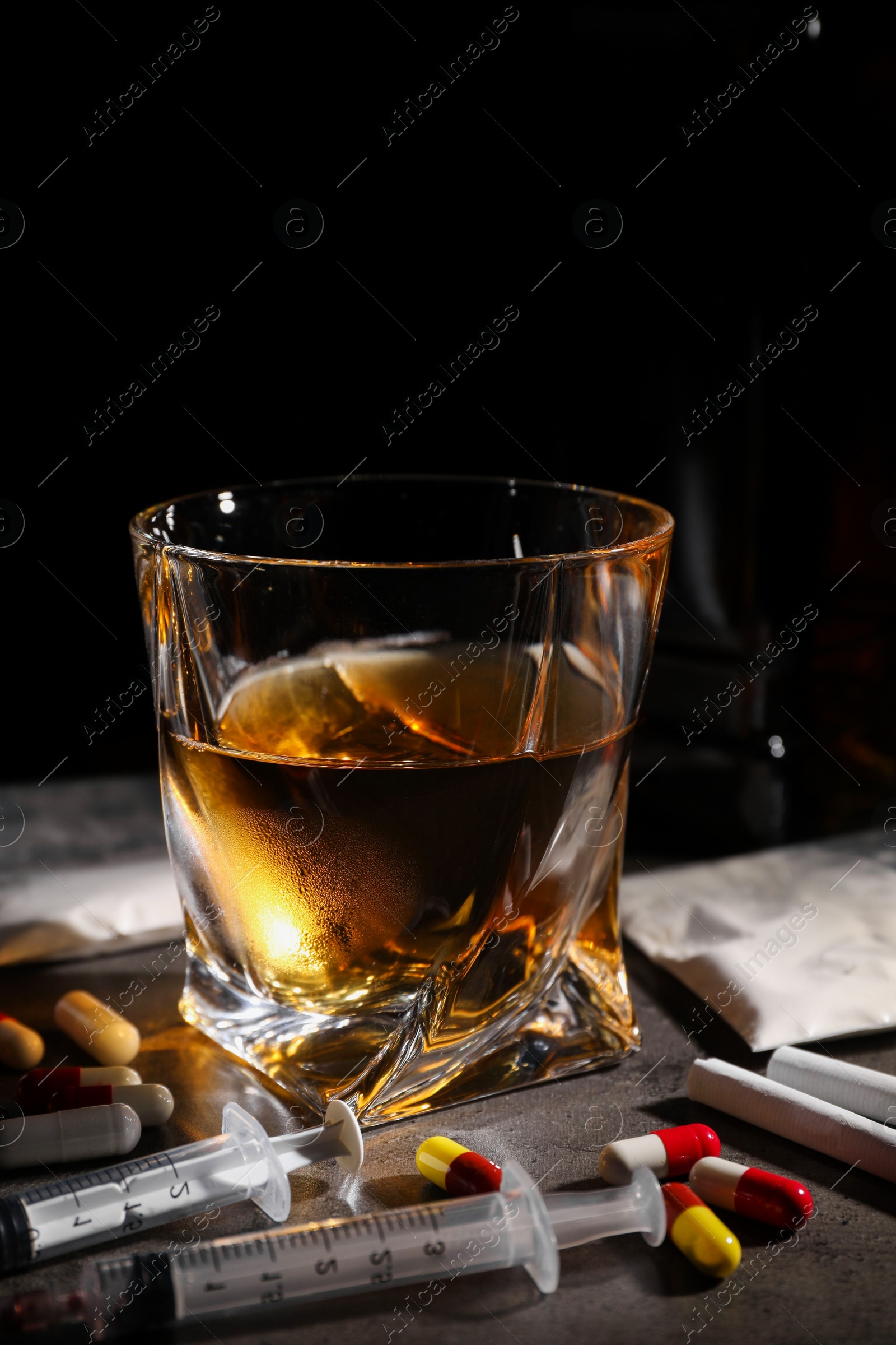 Photo of Alcohol and drug addiction. Whiskey in glass, syringes, pills and cocaine on grey table