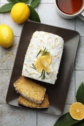 Photo of Tasty lemon cake with glaze, citrus fruits and tea on gray textured table, flat lay