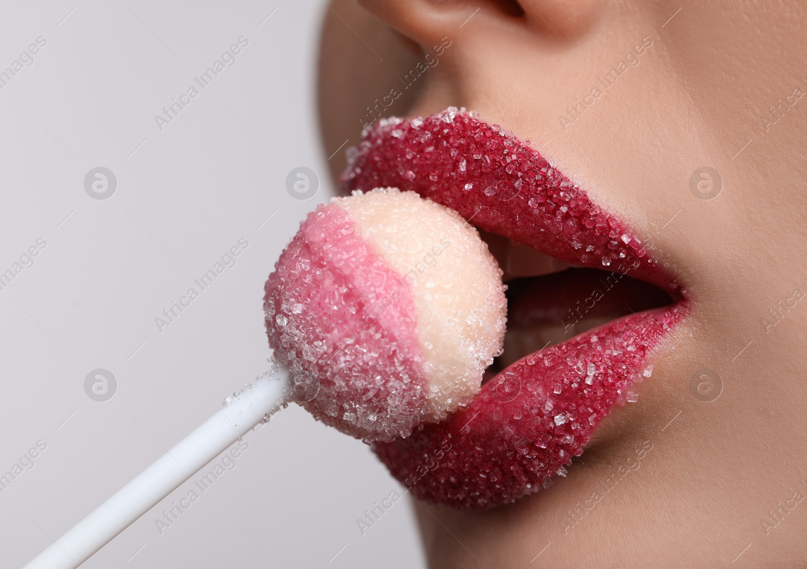 Photo of Young woman with beautiful lips covered in sugar eating lollipop on light background, closeup