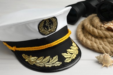 Peaked cap, rope, shells and binoculars on white wooden background, closeup