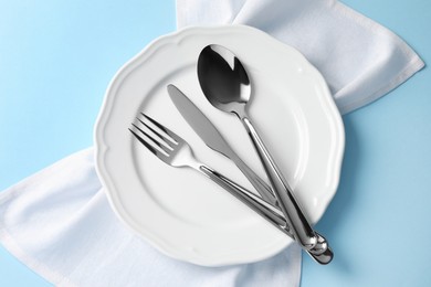 Stylish silver cutlery, plate and napkin on light blue background, top view