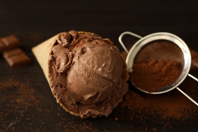 Photo of Delicious chocolate ice cream in wafer cone served on wooden table, closeup