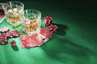Photo of Casino chips, dice, playing cards and glasses of whiskey on green table, space for text