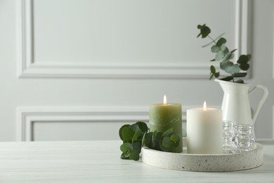Burning candles and branches of eucalyptus on white table indoors, space for text