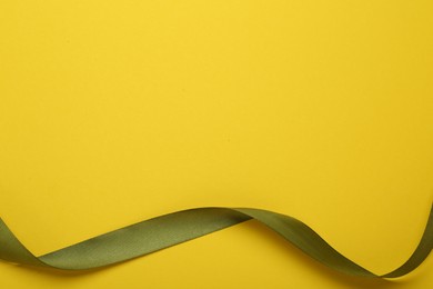Photo of Beautiful green ribbon on yellow background, top view. Space for text