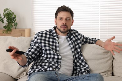 Emotional man with remote controller watching TV at home