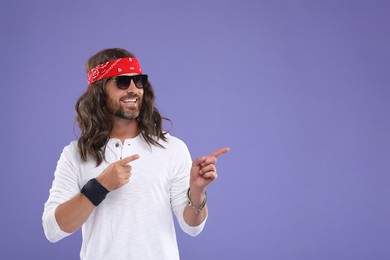 Photo of Stylish hippie man in sunglasses pointing at something on violet background, space for text
