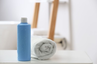 Photo of Bottle of bubble bath and towel on white table in bathroom, space for text