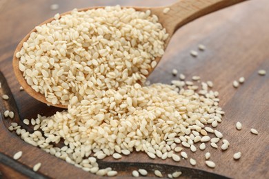 Photo of Spoon with sesame seeds on wooden board, closeup