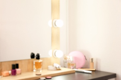 Photo of Blurred view of table with makeup products and mirror near white wall, closeup. Dressing room