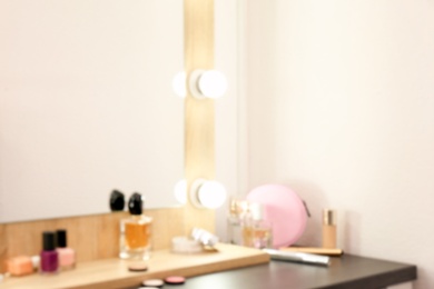 Blurred view of table with makeup products and mirror near white wall, closeup. Dressing room