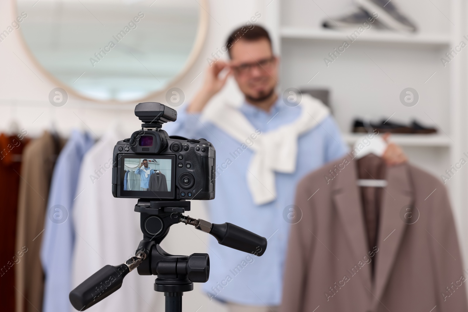 Photo of Fashion blogger showing clothes while recording video at home, focus on camera