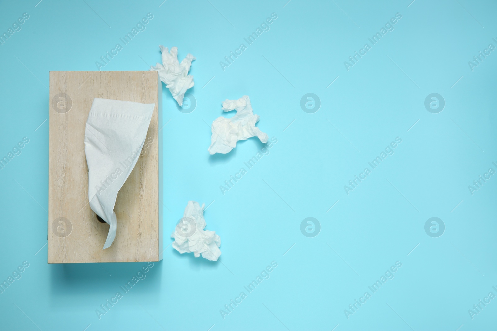 Photo of Used paper tissues and wooden holder on light blue background, flat lay. Space for text