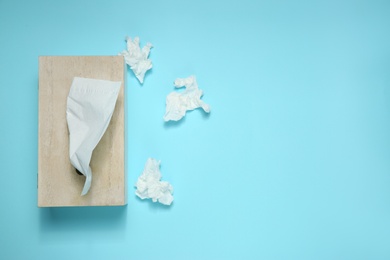 Photo of Used paper tissues and wooden holder on light blue background, flat lay. Space for text