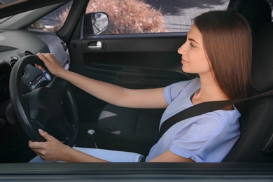 Young woman with fastened safety belt on driver's seat in car