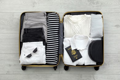 Open suitcase with clothes, passport and accessories on floor, top view