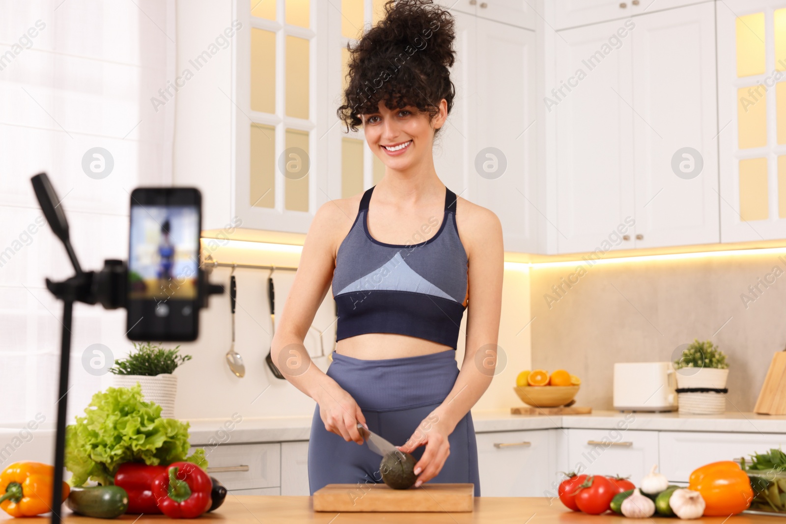 Photo of Smiling food blogger cooking while recording video in kitchen