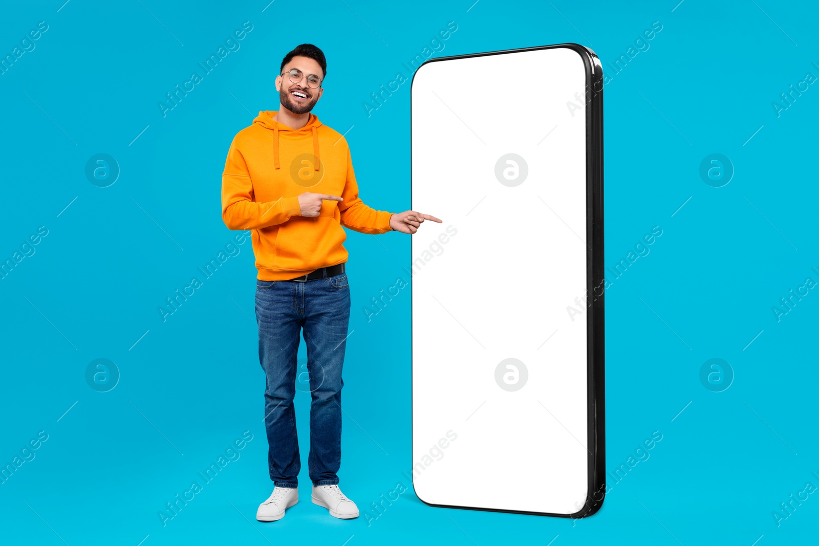 Image of Man pointing at huge mobile phone with empty screen on light blue background. Mockup for design