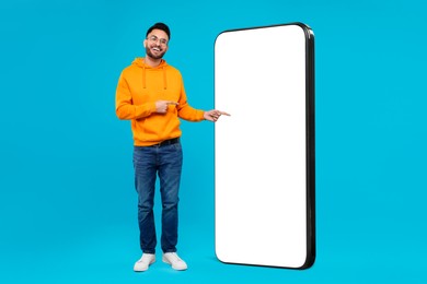 Man pointing at huge mobile phone with empty screen on light blue background. Mockup for design