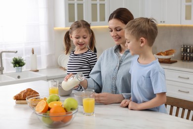 Photo of Mother and her little children having breakfast at table in kitchen