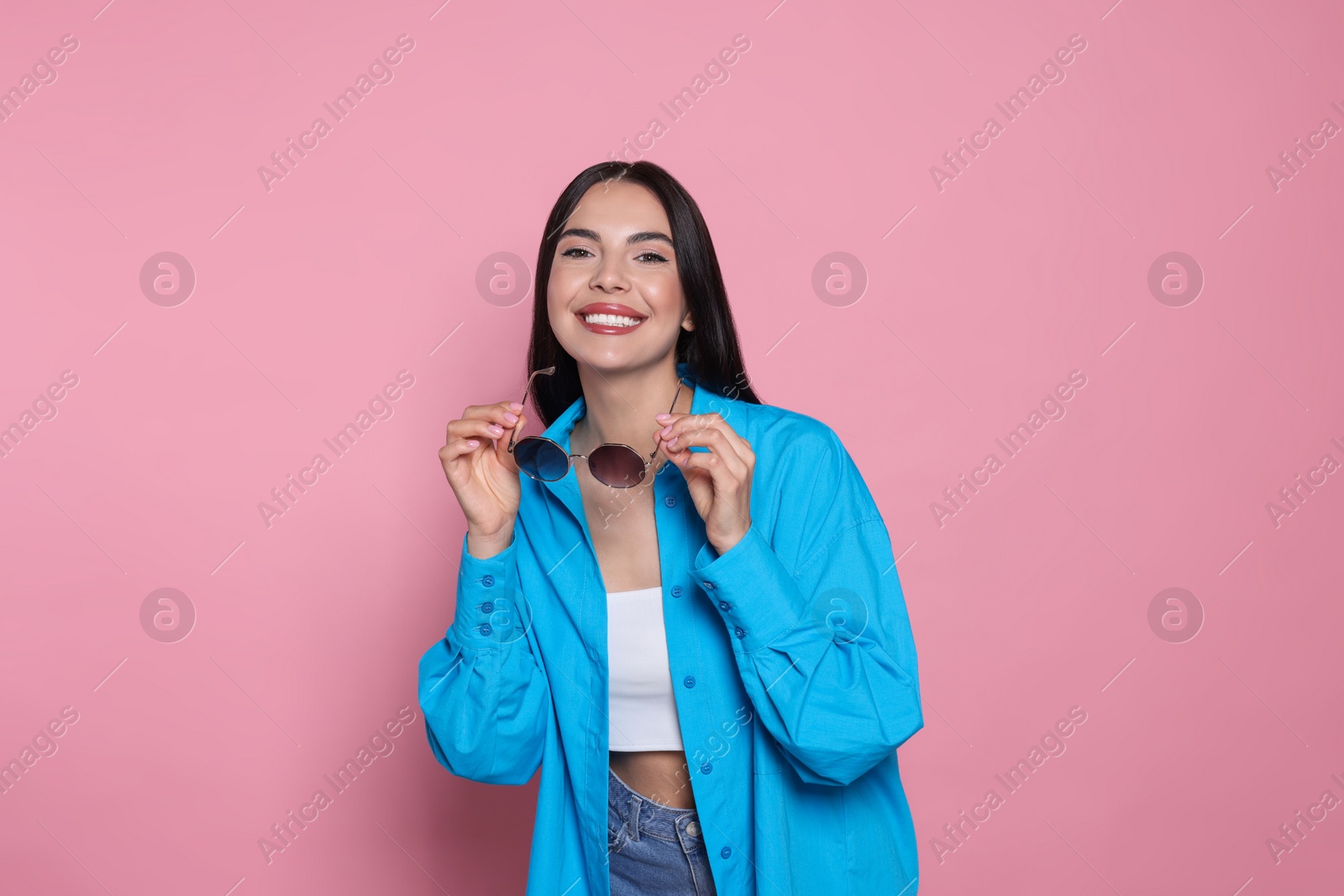 Photo of Attractive happy woman holding fashionable sunglasses against pink background. Space for text