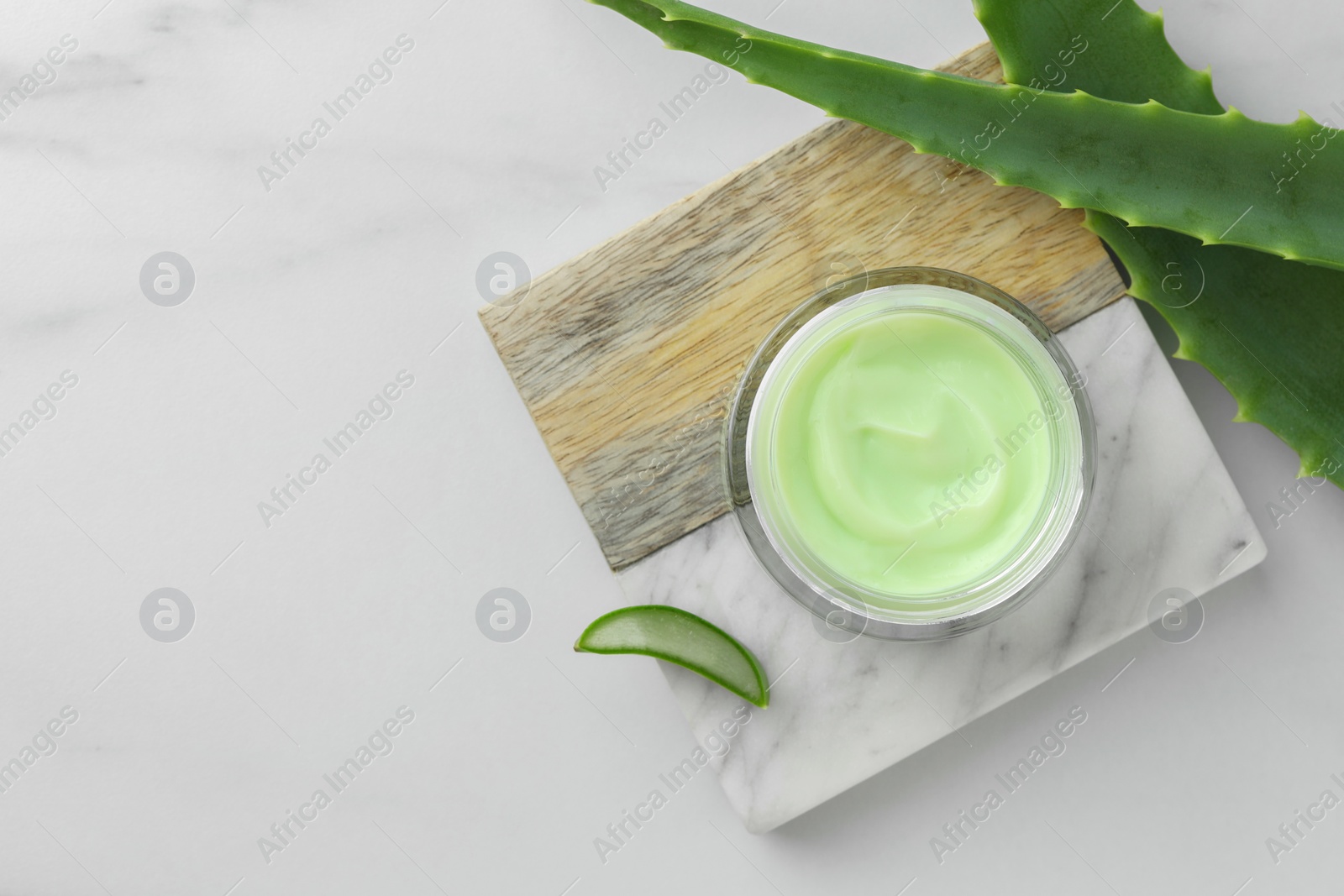 Photo of Jar with cream and cut aloe leaves on white marble table, flat lay. Space for text