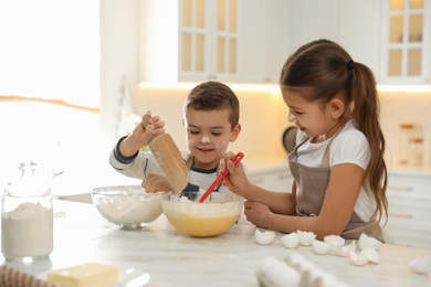 Photo of Cute little children cooking dough together in kitchen