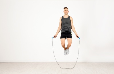 Photo of Full length portrait of young sportive man training with jump rope in light room