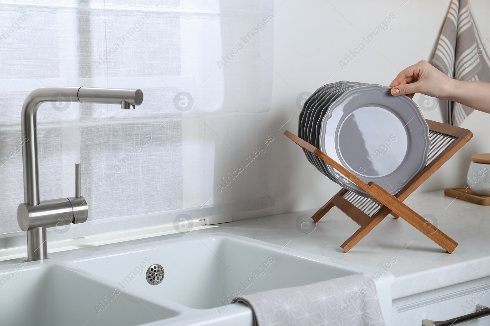 Photo of Woman taking grey plate from wooden holder in kitchen, closeup