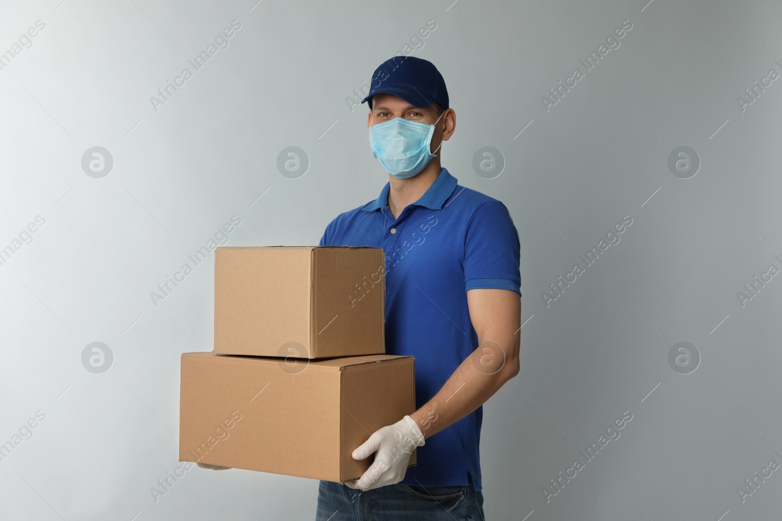 Photo of Courier in protective mask and gloves holding cardboard boxes on light background. Delivery service during coronavirus quarantine