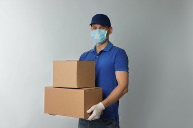 Courier in protective mask and gloves holding cardboard boxes on light background. Delivery service during coronavirus quarantine