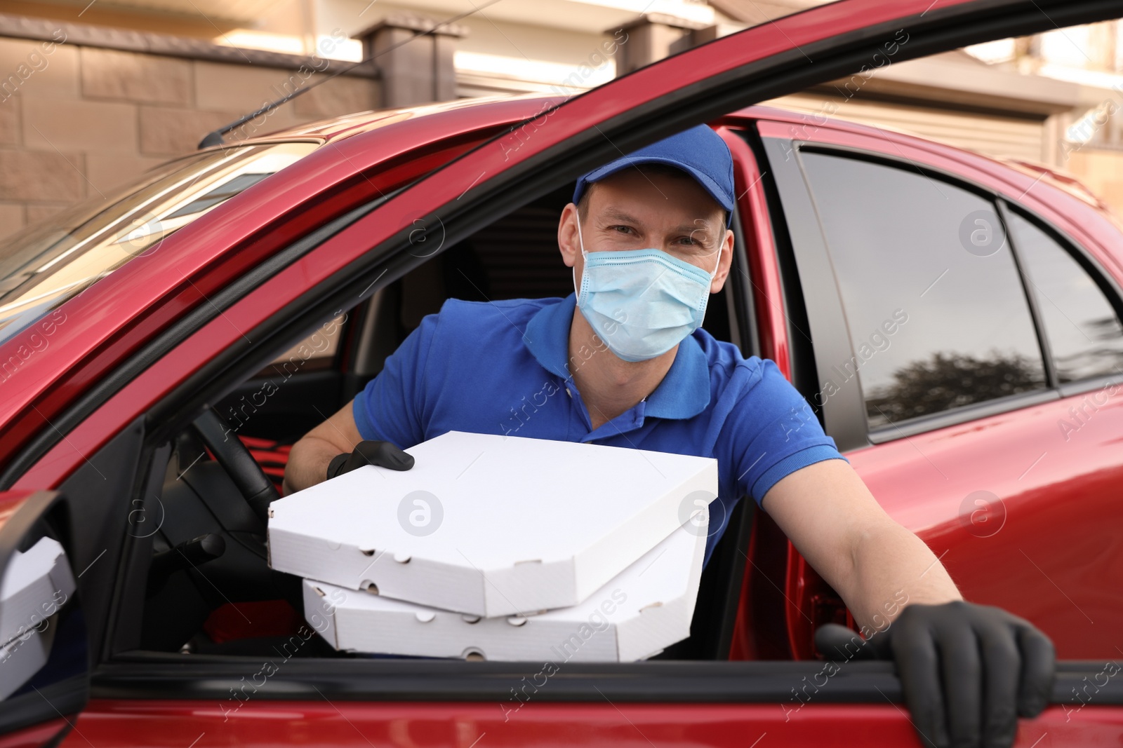 Photo of Courier in protective mask and gloves with pizza boxes getting out of car outdoors. Food delivery service during coronavirus quarantine