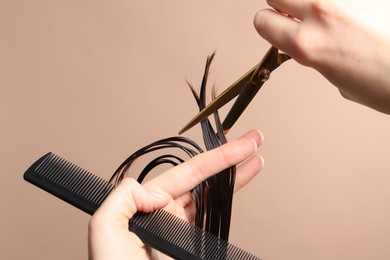 Hairdresser cutting client's hair with scissors on light brown background, closeup