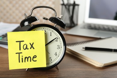 Photo of Alarm clock and reminder note with words Tax Time on wooden table. Space for text