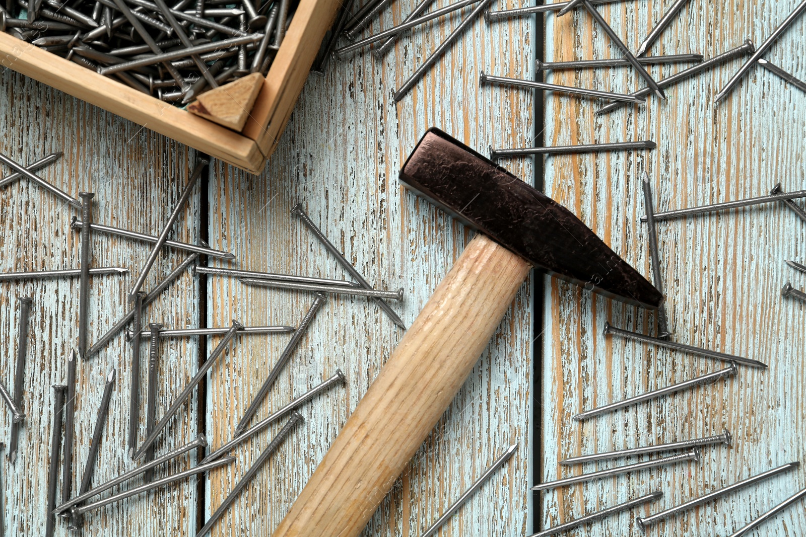 Photo of Hammer and metal nails on light blue wooden table, flat lay