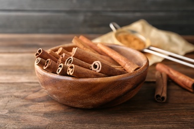 Photo of Bowl with aromatic cinnamon sticks on wooden table