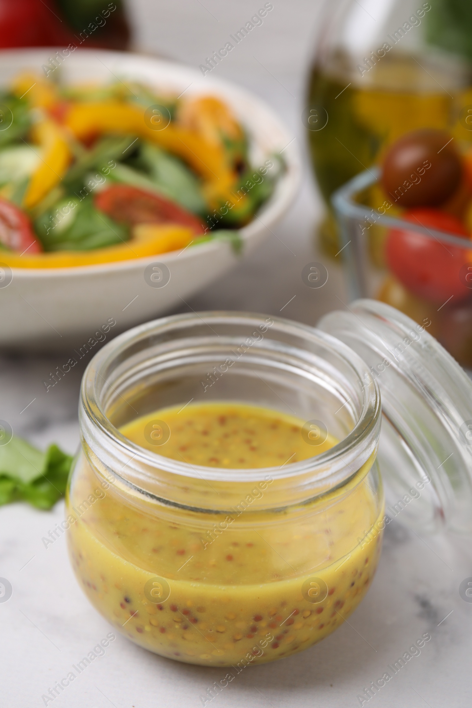 Photo of Tasty vinegar based sauce (Vinaigrette) in jar on white marble table, closeup