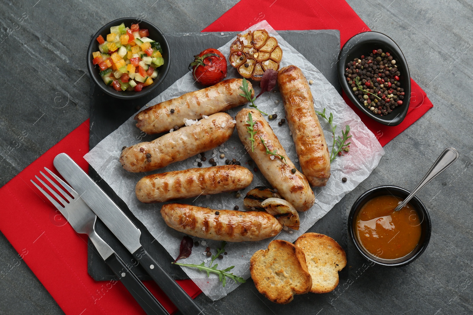 Photo of Tasty fresh grilled sausages served with vegetables on grey table, flat lay