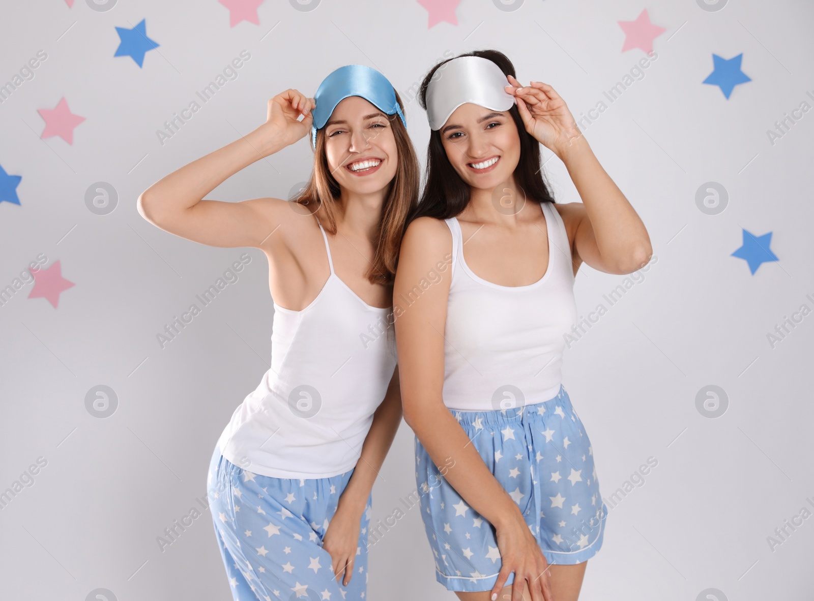 Photo of Beautiful women wearing sleeping masks on light grey background. Bedtime