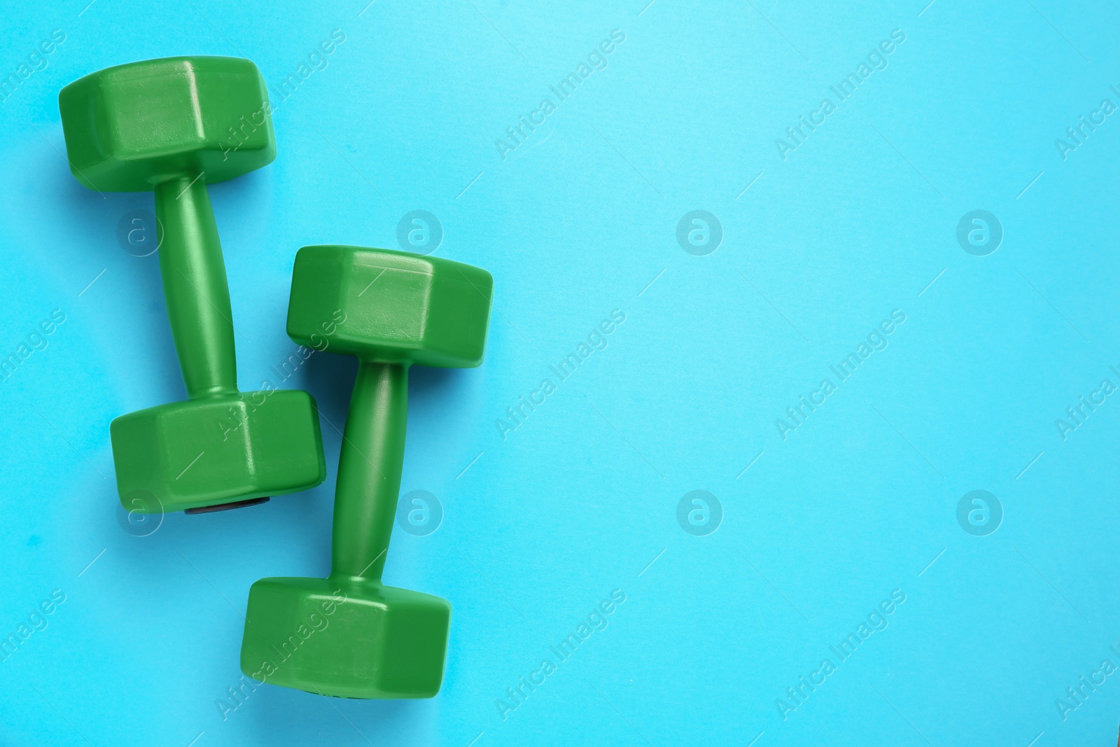 Photo of Green dumbbells on light blue background, flat lay. Space for text